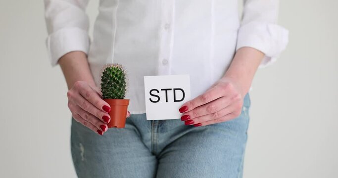 Woman holds cactus in pot and paper with STD inscription. Female person feels symptoms and pain due to sexually transmitted diseases slow motion