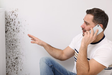 Mold removal service. Man talking on phone and looking at affected wall in room