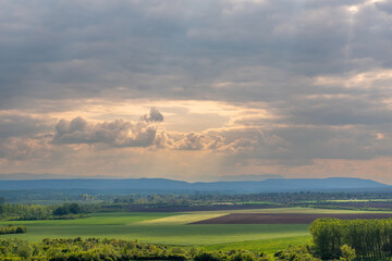 A cultivated field in early spring and a sky with dramatic clouds through which sunlight streams, Danube Plain, Bulgaria.