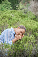 Brown-haired woman visits rosemary field enjoying smell of plants. Lady tourist enjoys exploring landmarks of picturesque seaside resort