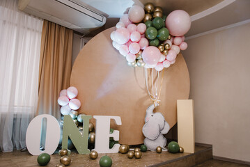 Birthday party for 1 year old girl or boy on background brown photo wall. Arch decorated pink, golden, green balloons, paper decor elephant, confetti. Reception. Celebration concept. Space for text.