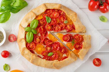 Tomatoes galette or pie with cheese and herbs on a white wooden background. Vegetarian dish. Selective focus.