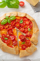 Tomatoes galette or pie with cheese and herbs on a white wooden background. Vegetarian dish. Selective focus.