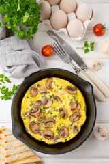 Omelette with mushrooms and herbs in a pan on a white wooden background. Healthy breakfast. Top view. Copy space.