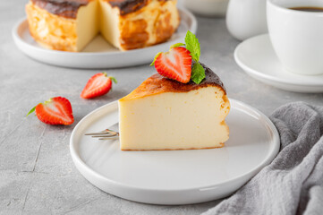 A piece of Basque burnt cheesecake or San Sebastian cheesecake with fresh strawberries on a white plate on a gray background. Selective focus. Copy space.