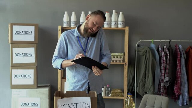 Young man working in charitable foundation. Volunteer calling use smartphone looking at donation box. Volunteer keeps track of donations