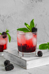 Blackberry Cocktail Gin and Tonic with fresh berries, ice and mint. Refreshing lemonade with blackberry and ice on a tile grey background. Drink photography