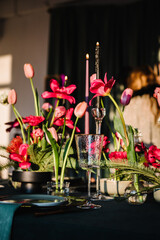 Family holidays in modern dining room. Stylish spring party. Wedding. Festive dinner table is served dishes, cutlery, decorated with flowers tulips and greenery, candle. Birthday celebration. Sunlight