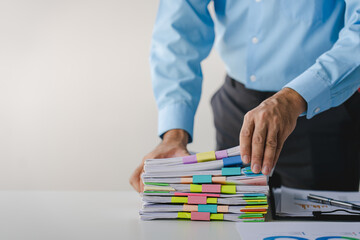 Businessman working on stacks of documents to search for information and check documents on office desk