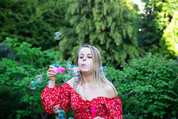 a woman in a red dress is playing with soap bubbles on the green lawn