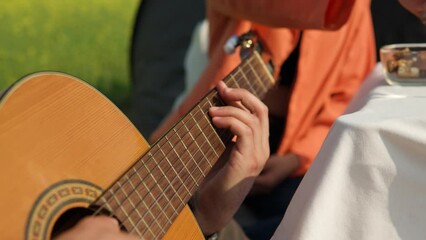 Close view man's hands playing acoustic guitar while girlfried eating chocolate on picnic in rural country field in slow motion
