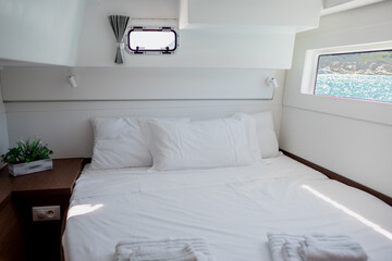Interior of bedroom in cabin of catamaran with comfortable bed with white bedclothes