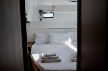 Interior of bedroom in cabin of catamaran with comfortable bed with white bedclothes