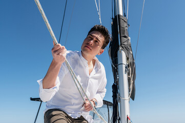 From below of concentrated male standing on deck of catamaran while pulling ropes and setting sail