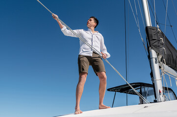 From below of concentrated male standing on deck of catamaran while pulling ropes and setting sail