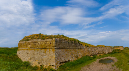 Fototapeta na wymiar old medieval fortress wall among green fields under blue cloudy sky, open air museum scene