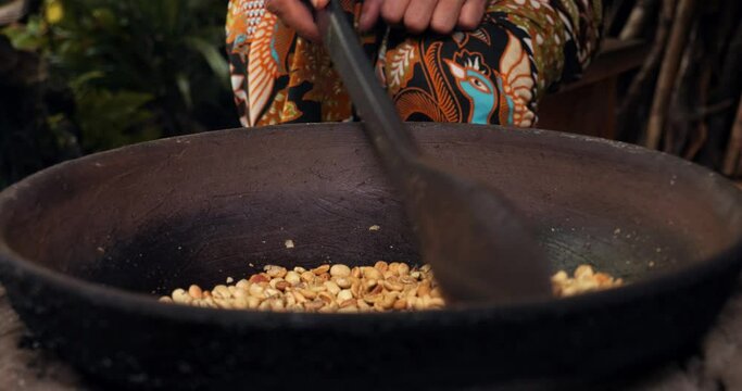 Close-Up Shot of Kopi Luwak Coffee Beans Roasting in Pot, Stirred with Wooden Spoon by Plantation Worker Dressed in Sarong