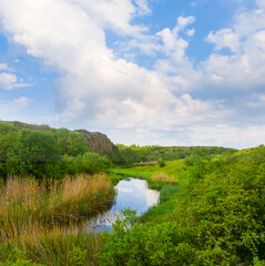 small calm river flow among green hills under cloudy sky