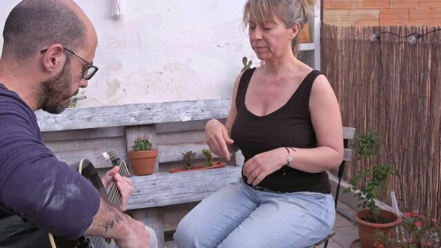 hombre y mujer practican con instrumento de cuerda, clases de guitarra en terraza