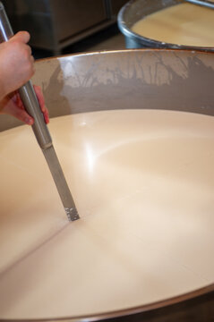 Cheesemaker cooking stirring italian bufalo organic milk in stainless steel caudrons, to produce ricotta cheese, italian food excellence worldwide export.