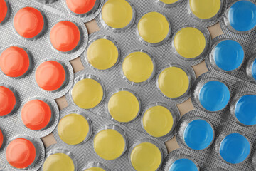 Blisters with colorful cough drops as background, top view