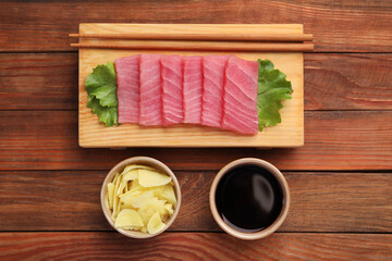 Tasty sashimi (pieces of fresh raw tuna), lettuce, soy sauce and ginger slices on wooden table,...