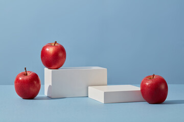 White podium in rectangle-shaped decorated with apples over a blue background. Apple (Malus...
