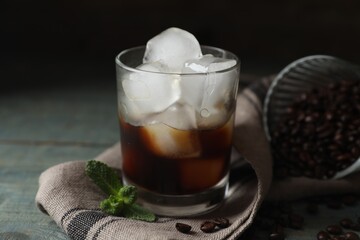 Glass of delicious iced coffee, beans and mint on light blue table, closeup