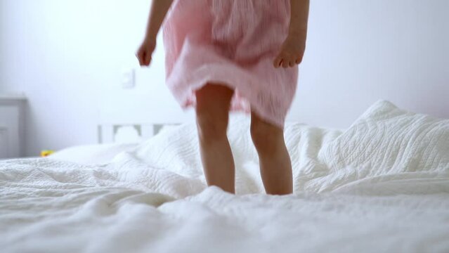 Preschooler girl in pink dress having fun and jumping on the bed at home