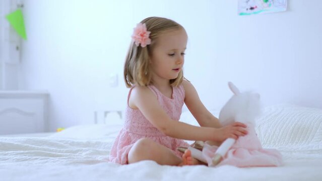 Adorable little girl in pink dress playing with unicorn. Kid having fun with soft toy. Child playing with stuffed toy