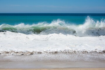 Fototapeta premium Closeup shot of waves crashing on the beach in the daylight