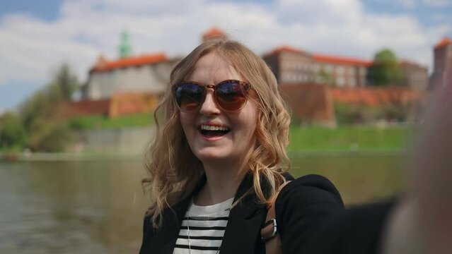Young happy blonde woman tourist with stylish clothes and sunglasses making selfie photo in front of the famous Wawel castle in Krakow city, Poland. High quality FullHD footage