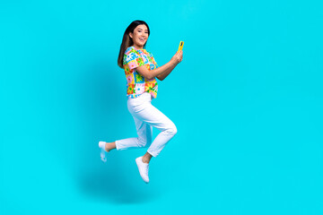Fototapeta na wymiar Full body photo of overjoyed funky lady jumping with phone blogger recording video her vacation memories isolated on cyan color background