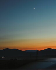 Vertical of mountain skyline against the sunset sky with a shiny half moon in the sky