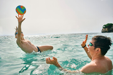 Happy family swim outdoors, father and son bonding, play ball, swim in the sea looking at view enjoying summer vacation. Togetherness Friendly concept
