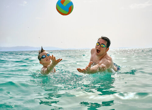 Happy family swim outdoors, father and son bonding, play ball, swim in the sea looking at view enjoying summer vacation. Togetherness Friendly concept