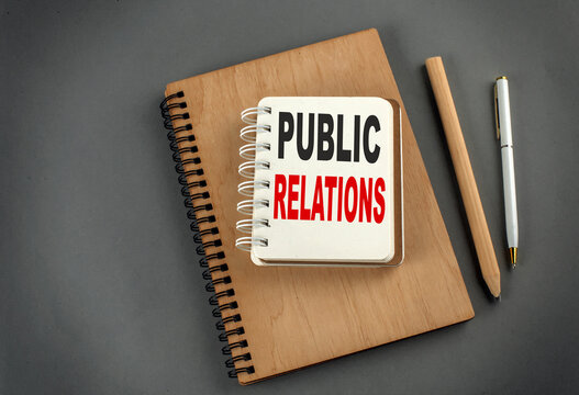 PUBLIC RELATIONS text on notebook with pen and pencil on grey background