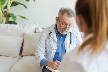 Senior man doctor examining yound woman in doctor office or at home. Girl patient and doctor have consultation in hospital room. Medicine healthcare medical checkup. Visit to doctor