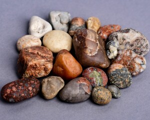 Natural stones in brown white and gray colors, placed by each other on a mauve purple background