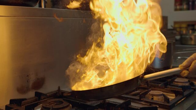 Chef cooking food in pan with fire flame, slow motion