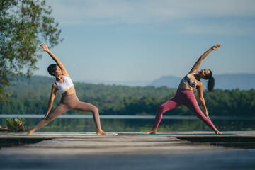Group of people doing yoga exercises by the lake at morning outdoor, Woman practicing yoga in lotus...