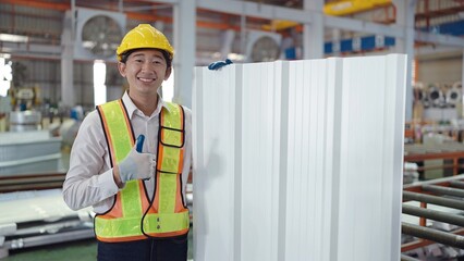 Portrait of asian engineer men in safety uniform holding metal sheet roof silver colour looking at camera while standing with thumbs up at industrial factory