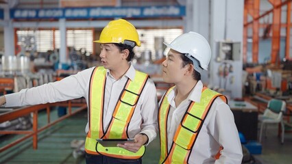 Two professional asian engineers men in safety uniform holding tablet working and discuss while walking at industrial factory. Manufacturing industry concept