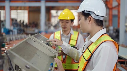 Two professional engineers men in safety uniform working and checking or maintenance machine in industry factory. Engineers men inspecting the settings of the machinery