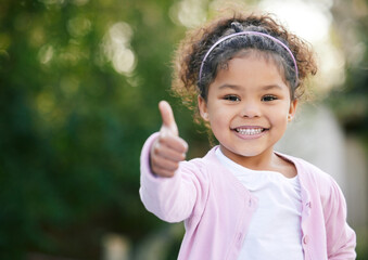 Happy, thumbs up and portrait of a child in a garden with a smile, emoji and positive emotion. Happiness, excited and cute girl kid standing in outdoor park with approval or satisfaction hand gesture