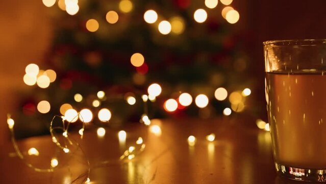 Slow-motion view of hot tea in a glass cup on a table with a background of Christmas bokeh lights
