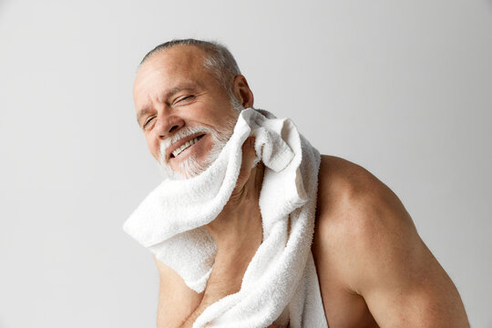 Portrait of satisfied, handsome, smiling man doing face care morning routine against grey background. Concept of male beauty, face and skin care, daily procedures, age, well-being and health