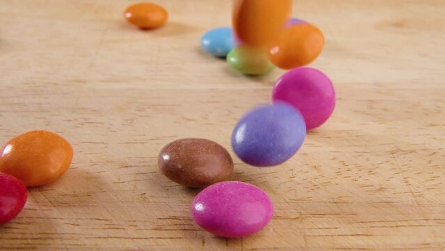 Slow motion of colorful candies falling on the wooden kitchen board surface on blurred background