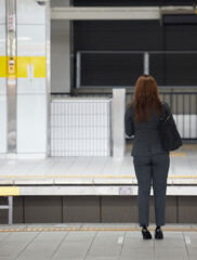 駅のホームで電車待ちのビジネス女性の後姿