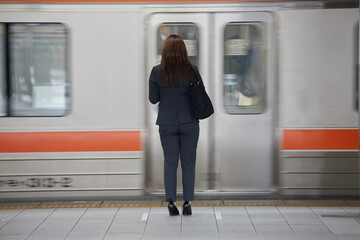 駅のホームで電車待ちのビジネス女性の後姿